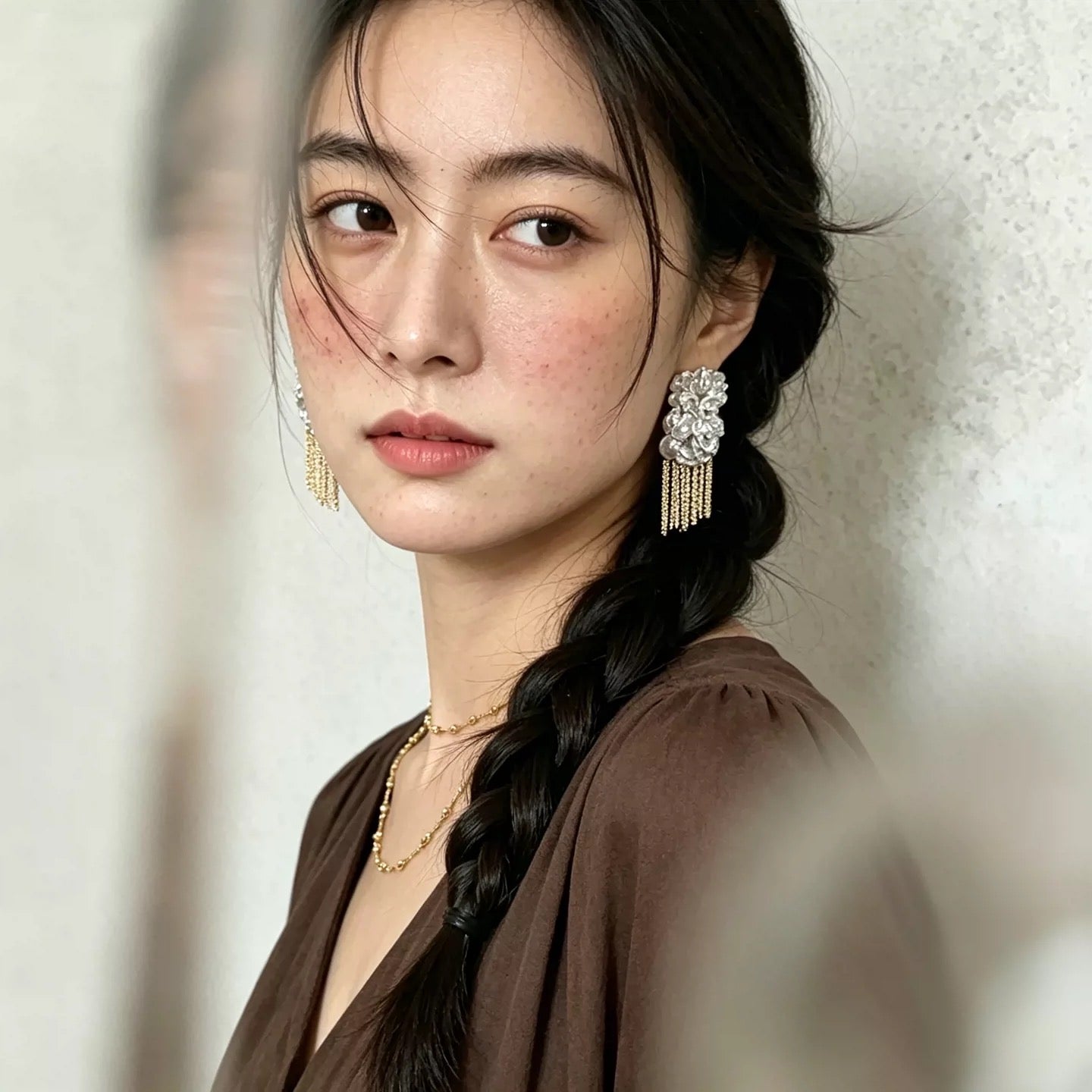 Woman wearing crystal flower tassel earrings and gold necklace, braided hairstyle, dark brown wide-sleeve top