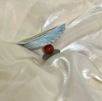 Blue iridescent mussel shell resting on shimmery white satin fabric alongside a deep red carnelian bead and a small green jade stone, styled as a natural wellness flat lay