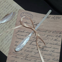 Mother-of-pearl butter spreader and shell fish brooch resting on vintage handwritten letters tied with a satin ribbon, stamped with E. Moyle Lion Hotel postmark on black background