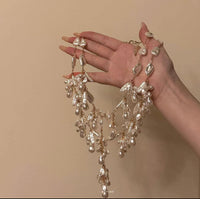 Hand holding a luxurious baroque pearl tassel necklace with gold chain, featuring cascading irregular freshwater pearls against a beige background