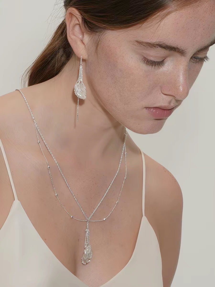 Model wearing baroque pearl drop earring and layered silver back necklace with pearl pendant, styled with open-back dress
